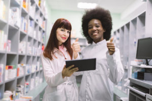 Two pharmacy tech standing pharmacy giving thumbs up.